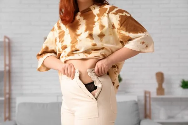 Image of woman trying to do her trousers up after pregnancy weight gain Littlehampton